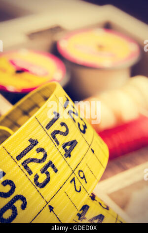 Gelbe Schneider-Maßband hautnah mit Spulen des Threads im Retro-Vintage-Stil. Vertikales Bild. Stockfoto
