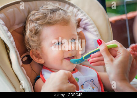 Eine Mutter füttert ihr Baby Boy mit Löffel im Freien. Stockfoto