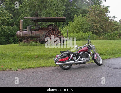 Ein Motorrad geparkt in der Nähe einer alten verrosteten Ackerschlepper, in der Nähe der Blue Ridge Parkway in Virginia, USA an einem Sommertag. Stockfoto