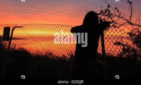 Silhouette der Person stützte sich auf Metallzaun bei Sonnenaufgang Blick auf Meer, Malibu, California, Amerika, USA Stockfoto