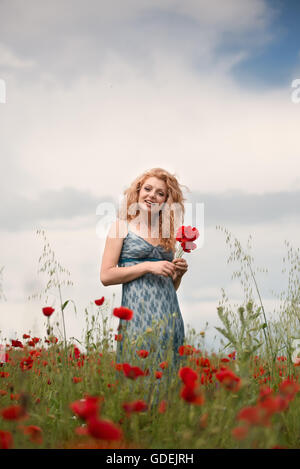 Lächelnde Frau in Mohnfeld halten Blumen Stockfoto