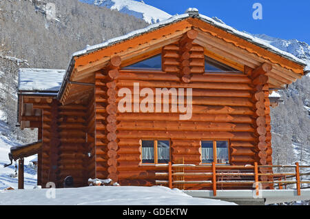 Eine alpine Blockhütte mit Schnee bedeckt, Berge und Wälder im Hintergrund Stockfoto