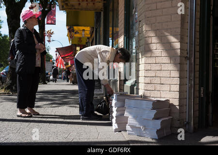 Asiatischer Mann einen Stapel Zeitungen durchsuchen. Vancouver Chinatown, Britisch-Kolumbien. Stockfoto