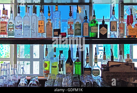 In einem Regal in einer gehobenen Lounge befinden sich farbenfrohe Flaschen mit Getränken und Likören für Erwachsene mit gestapelten Cocktail- und Weingläsern. Stockfoto