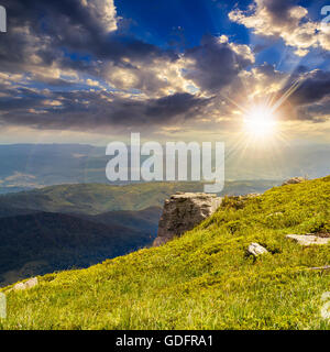 sehen Sie sich auf hohe Berge aus Hügel bedeckt mit Rasen mit einigen Steinen am Rande im Abendlicht Stockfoto