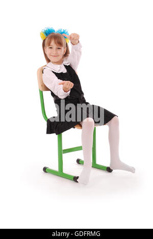 Schulmädchen, die sitzen auf dem Stuhl zeigt Daumen isoliert auf weißem Hintergrund Stockfoto