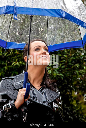 Attraktive junge Frau gekleidet für Nasses Wetter in glänzend schwarzem pvc Regenmantel und Schirm Stockfoto