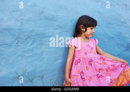 Schuss von kleinen Mädchen im rosa Kleid stehen gegen blaue Wand. Stockfoto