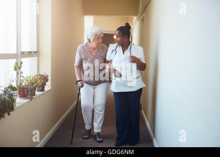 Ältere Frau mit Gehstock von einer Krankenschwester zu Hause geholfen. Volle Länge-Schuss der Ärztin mit älteren Patienten ein Stockfoto