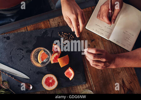 Draufsicht der Zutaten für einen Cocktail mit Barkeeper Notizen zu machen. Schneiden Sie, Grapefruit und schwarzem Pfeffer auf Schneidebrett Stockfoto