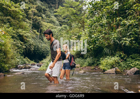 Paar Hand in Hand als der Mann hilft seiner Freundin über den Bach ihren Wanderweg. Mann und Frau im Wald, Natur Hallo Stockfoto