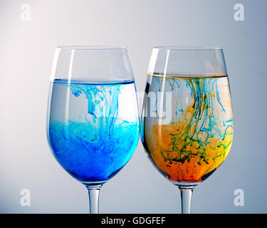 Zwei Gläser Wein mit Wasser gefüllt und Verbreitung rote, gelbe und blaue Tinte Stockfoto