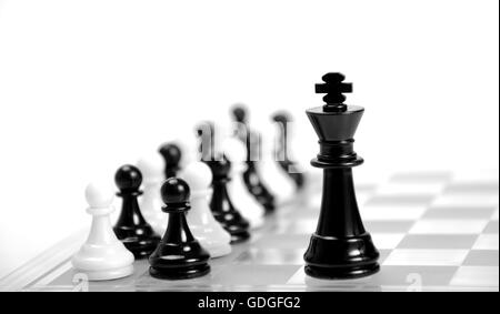Weißen und schwarzen König auf dem Schachbrett gegen einander, schwarzen und weißen Figuren im Hintergrund. Stockfoto