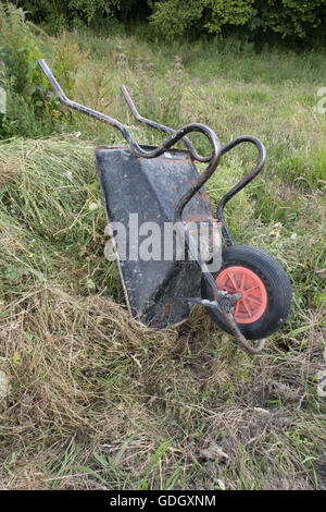 Eine umgekehrte Schubkarre auf einem Komposthaufen von Gras und Unkraut. Im Hochformat aufgenommen. Stockfoto