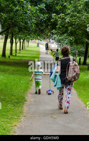 Eine Frau geht durch Prospect Park in Reading mit ihren zwei jungen Enkel drücken ihre Roller. Stockfoto