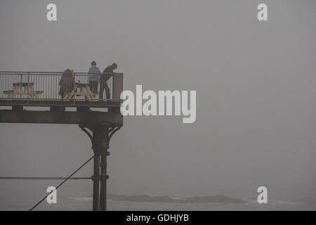 Aberystwyth Wales UK, Sonntag, 17. Juli 2016 UK Wetter: Menschen auf dem Meer Pier auf dicken Nebel nebligen Grau bedeckt Sonntag Nachmittag im Juli "Sommer". Das Wetter wird voraussichtlich am Dienstag mit Temperaturen bis 28 º steigen voraussichtlich drastisch verbessern Celsius Credit: Keith Morris / Alamy Live News Stockfoto