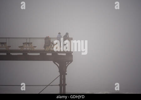 Aberystwyth Wales UK, Sonntag, 17. Juli 2016 UK Wetter: Menschen auf dem Meer Pier auf dicken Nebel nebligen Grau bedeckt Sonntag Nachmittag im Juli "Sommer". Das Wetter wird voraussichtlich am Dienstag mit Temperaturen bis 28 º steigen voraussichtlich drastisch verbessern Celsius Credit: Keith Morris / Alamy Live News Stockfoto