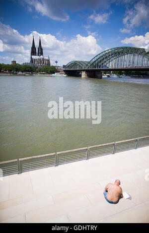 Ein Mann sonnen sich und liest ein Buch über den Rhein Boulevard in Köln, Deutschland, 18. Juli 2016. Foto: ROLF VENNENBERND/dpa Stockfoto