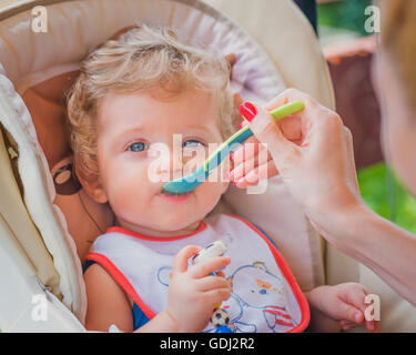 Eine Mutter füttert ihr Baby Boy mit Löffel im Freien. Stockfoto