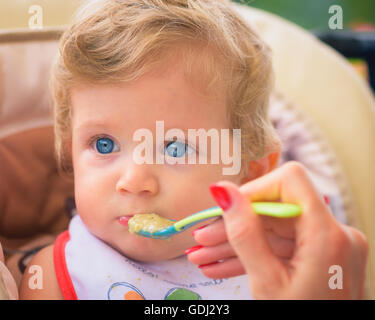 Eine Mutter füttert ihr Baby Boy mit Löffel im Freien. Stockfoto