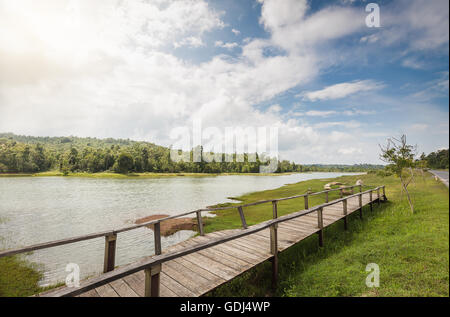 Holzbrücke über Überschwemmungsgebiet des großen Sees die grünen Rasen Land verbinden, daß Wald mit sonnigen blauen Himmel als Hinterg Stockfoto