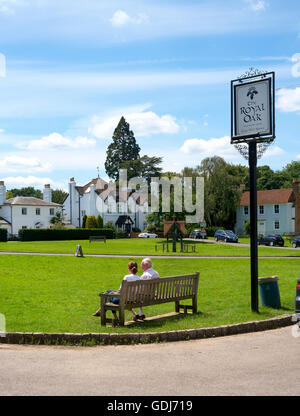 Der Dorfplatz von Brockham, Surrey, UK - ein Mann und eine Frau sitzen auf einer Bank vor The Royal Oak pub Stockfoto