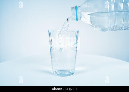 Gießen Wasser aus der Flasche ins Glas auf blauem Hintergrund Stockfoto