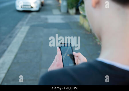 Teenager mit einem iPhone auf der Straße, augmented-Reality-Spiel Pokemon Go spielen Stockfoto