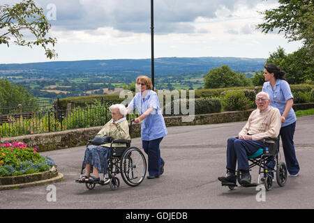 Ältere Menschen, die im Juli im Rollstuhl ausgefahren werden, um die frische Luft im Park Walk, Shaftesbury, Dorset, Großbritannien zu genießen - soziale Betreuung Stockfoto