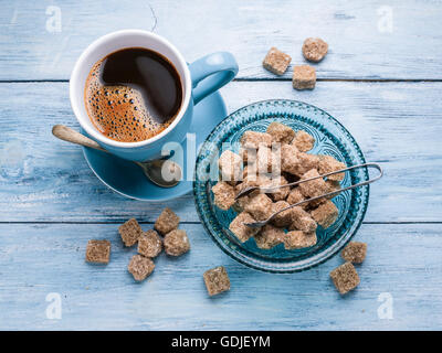 Tasse Kaffee, Milchkännchen und Rohrzucker Würfel auf alten blauen Holztisch. Stockfoto