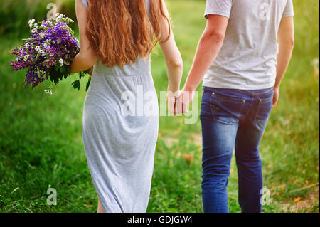 Paare, die auf Wiese mit Blumenstrauß Stockfoto