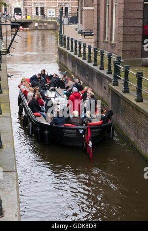 Ein kleines Boot voller Menschen, so dass es auf eine schmale Strecke am Kanal in Amsterdam, Holland, Niederlande. Stockfoto