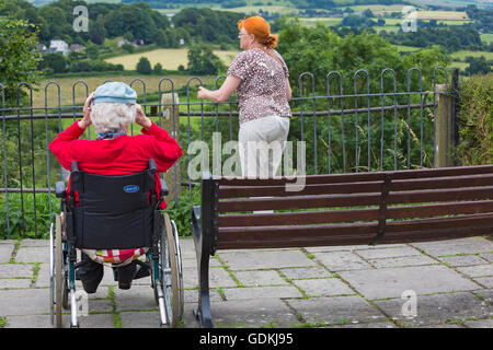 Ältere Frau im Rollstuhl und Frau mit orangen Haaren genießen die Aussicht vom Park zu Fuß, Shaftesbury, Dorset im Juli Stockfoto