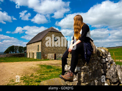 Teenager-Mädchen sitzen auf einer Trockenmauer in der Nähe einer Scheune auf einem Land gehen im Peak District Nationalpark Derbyshire England UK Stockfoto