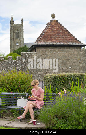 Junge Frau beim Mittagessen im Park Walk mit Holy Trinity Church in der Ferne, Shaftesbury, Dorset im Juli Stockfoto