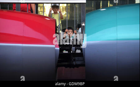 Tokio, Japan. 16. Juli 2016. Schlepptau jungen steht in der Nähe von den Gleisen, Blick auf die High-Speed-Smaragd Grün E5 Tohoku Shinkansen (Bullet Train) und E6 Serie Shinkansen (rot) an der Tokio Station in Tokio. Shinkansen E5 kann top-Geschwindigkeit von 320 km/h (fast 200mph), und auch manchmal '' Hayabusa'' (Falcon) nennen. Der E5 ist eines der Hochgeschwindigkeitszüge im Einsatz und es ist gefüllt mit modernster Technologie, um sicherzustellen, dass es sowohl umweltfreundlich als auch Ruhe und trotz seiner hohen Geschwindigkeit glatt ist. 10. Juli 2016. Foto von: Ramiro Agustin Vargas Tabar (Kredit-Bild: © Ramiro Agustin Vargas Stockfoto