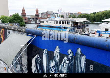 Ein Kunstwerk auf der Berliner Mauer an der East Side Gallery in Berlin, Deutschland, 19. Juli 2016 erneuert. Im Hintergrund auf der linken Seite sieht man die Oberbaumbrücke über die Spree. Seit ein paar Monaten wurde das Denkmal an der ehemaligen innerdeutschen Grenze repariert und renoviert durch zahlreiche beschmieren auf das Kunstwerk. Der Zaun ist sollen Besucher der Malerei vor erneuten Schaden zu schützen. Die lokale Verwaltung Büro Friedrichshain-Kreuzberg plant weiterhin das Kunstwerk zu schützen, selbst nach den Renovierungsarbeiten. Foto: Rainer Jensen/dpa Stockfoto