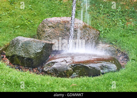 Große Menge an Wasser an eine Kette von Metallringen, die Landung auf großen Granitfelsen durch Starkregen Stockfoto