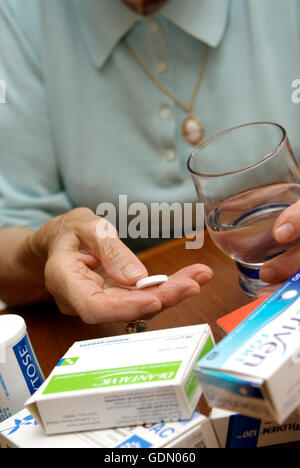 Hände einer älteren Frau hält eine Pille und ein Glas Wasser Stockfoto