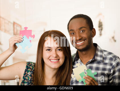 Interracial charmante Frau umarmen freundlich, große Puzzleteile hochhalten und glücklich Interaktion mit Spaß, verschwommen Studio-Hintergrund Stockfoto