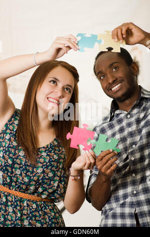 Interracial charmantes Paar lässige Kleidung hält große Puzzleteile und Interaktion glücklich, weiße Studio-Hintergrund Stockfoto