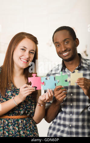 Interracial charmantes Paar lässige Kleidung hält große Puzzleteile und Interaktion glücklich, weiße Studio-Hintergrund Stockfoto