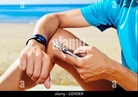 Nahaufnahme eines jungen Mannes, die Synchronisierung von seinem Smartphone und seine Smartwatch Sportkleidung tragen Stockfoto