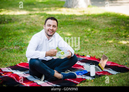 junger Geschäftsmann Essen brachte er ein Lunchpaket von zu Hause aus genießen. Mittags im Park im Freien. Stockfoto