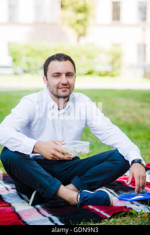 junger Geschäftsmann Essen brachte er ein Lunchpaket von zu Hause aus genießen. Mittags im Park im Freien. Stockfoto