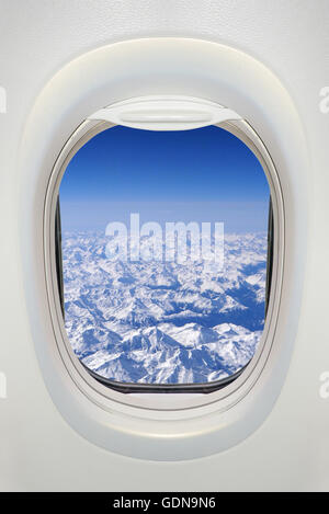 Fenster eines Flugzeugs von innen, Blick auf verschneiten Bergen (Alpen) Stockfoto