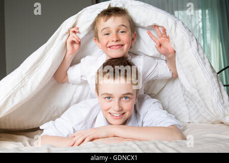 Junge im Bett unter einer weißen Decke Tagesdecke versteckt. Stockfoto