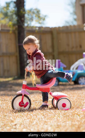 Weiblichen Kleinkind auf Dreirad im Garten spielen Stockfoto
