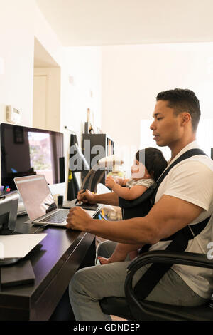 Vater mit Baby Carrier, arbeiten am laptop Stockfoto