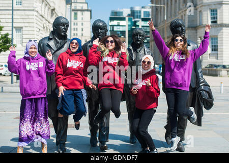 Eine Gruppe von glücklichen jungen Studenten der verschiedenen ethnischen Minderheiten Aufspringen vor den Beatles Statuen in Liverpool UK Stockfoto